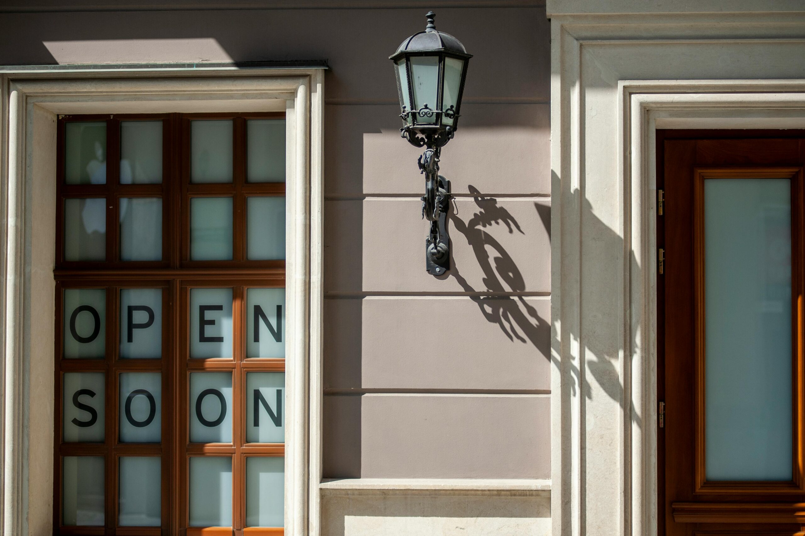 Charming facade in Lviv, featuring wooden windows and a classic lantern casting a shadow. "Open soon" sign adds intrigue.