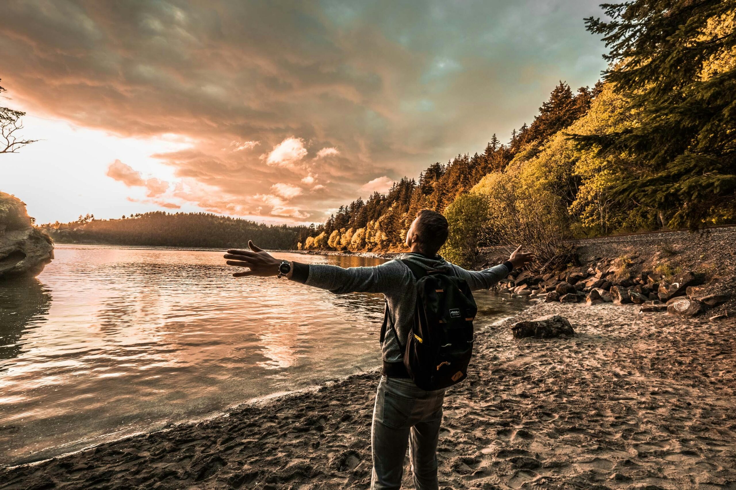 Man with arms outstretched, enjoying a scenic sunset by a lakeside in Bellingham, WA.